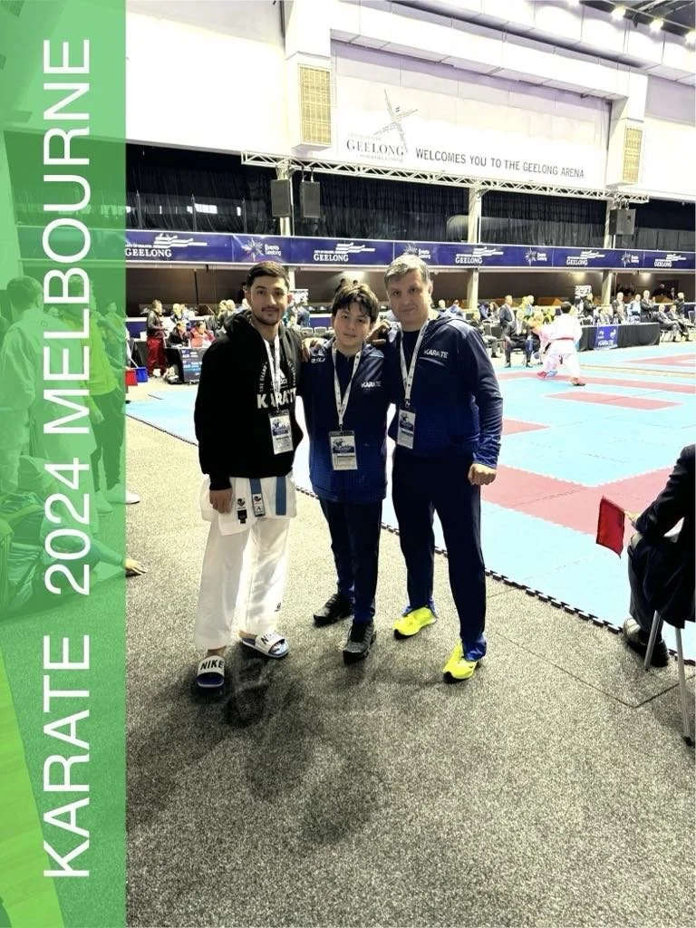 Three male karate competitors standing together at the 2024 Melbourne Karate event in Geelong Arena, with a tatami mat area in the background and spectators watching.