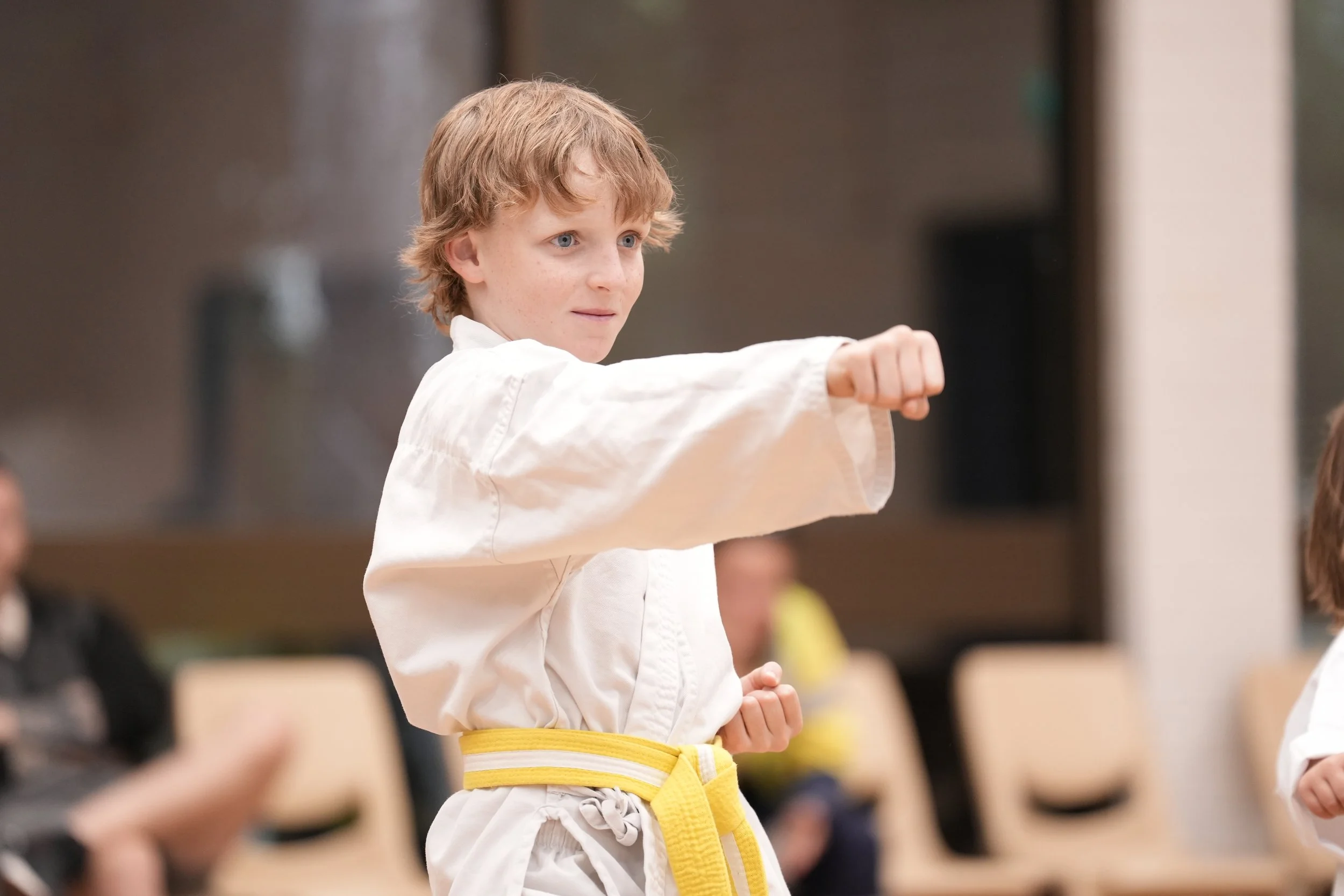Young boy in a karate gi with a yellow belt practicing martial arts in a dojo.
