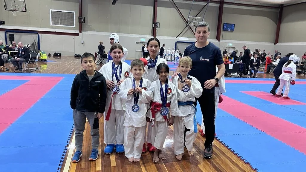 Group of young martial artists with medals and their coach in a gymnasium, celebrating after a competition.