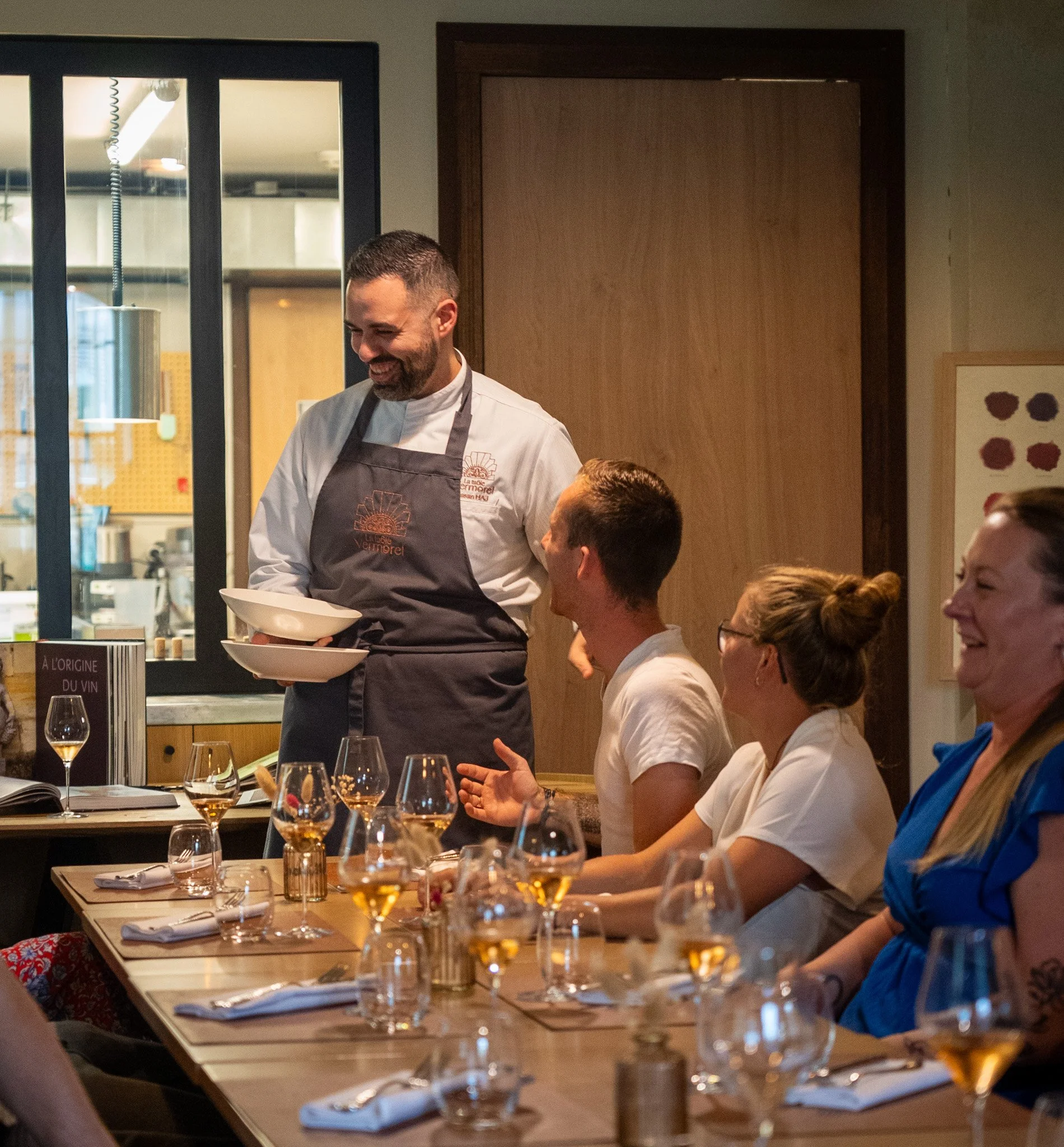 Un chef en train de servir un repas à une table de personnes dans un restaurant. Les convives sont assis, souriants et discutant dans une ambiance chaleureuse.