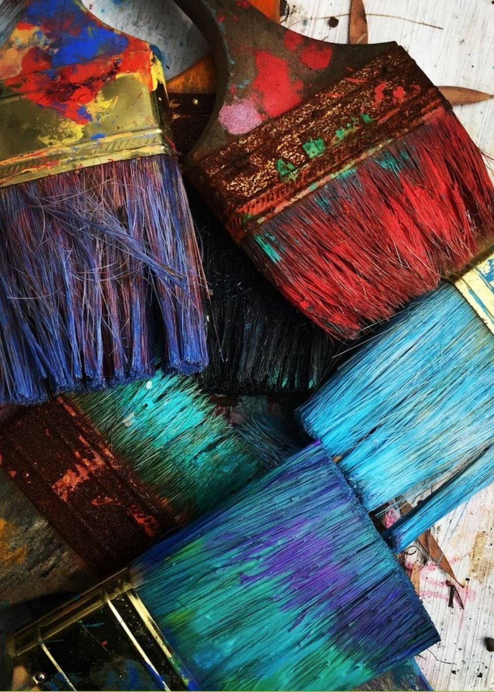 Several paintbrushes with colorful and splattered paint on their bristles and handles.