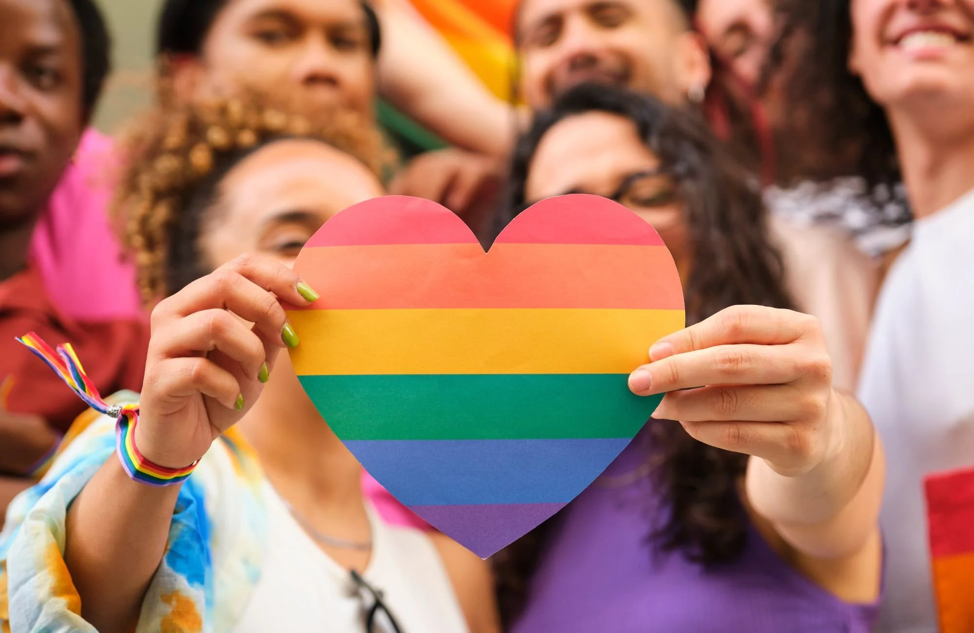 Two queer people holding up a rainbow color heart at a pride parade.