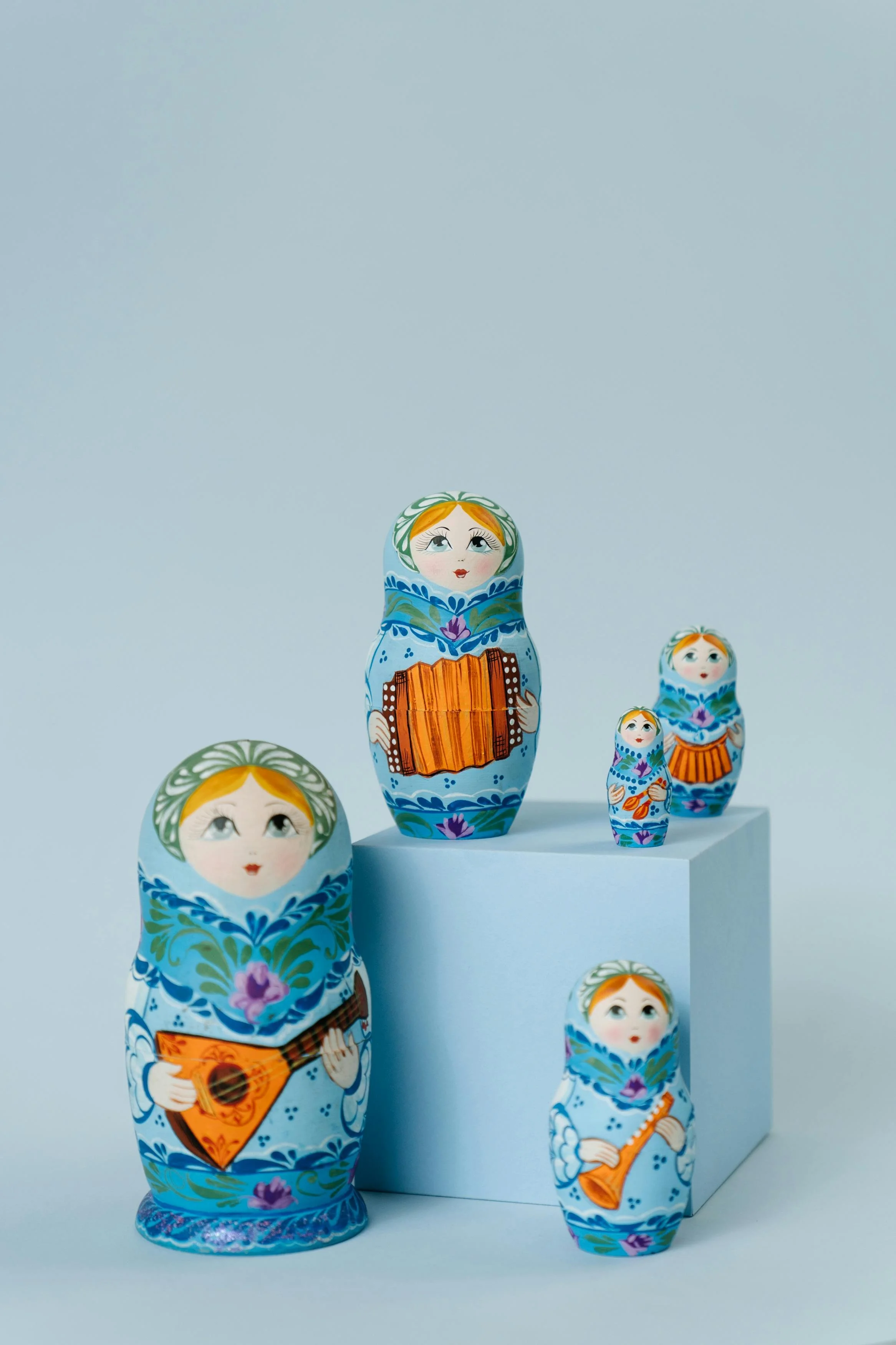 Set of five traditional Russian nesting dolls, decorated as women playing musical instruments, arranged on a white surface with a white block background.