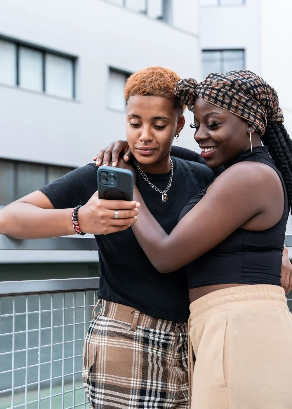 A picture of a BIPOC, gender expansive couple, smiling and looking at a smart phone.