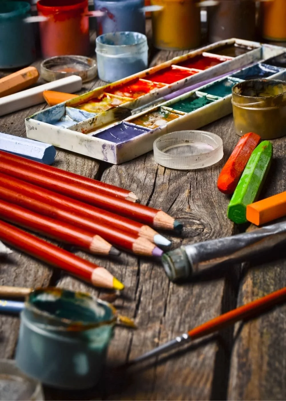 A picture of art supplies including colored pencils, a water color set and pastels.