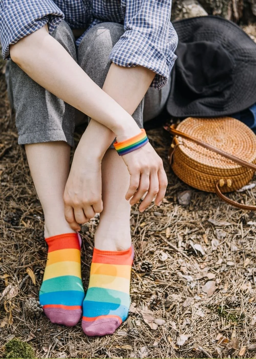 A picture of a queer adult with rainbow socks, sitting on grass.