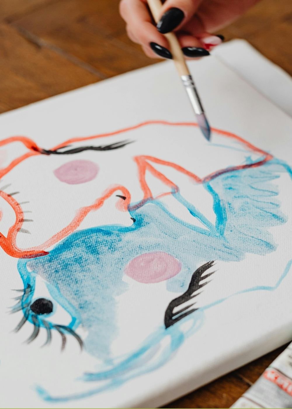 A hand painting a watercolor picture of a face in blue and orange. A self-portrait art therapy prompt.