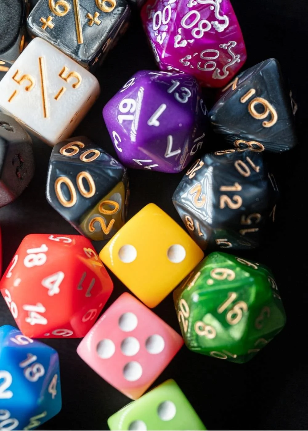 A collection of colorful polyhedral and six-sided dice used for tabletop role-playing games, including d20s, d12s, d10s, d8s, d6s, and a d4, arranged on a black surface.