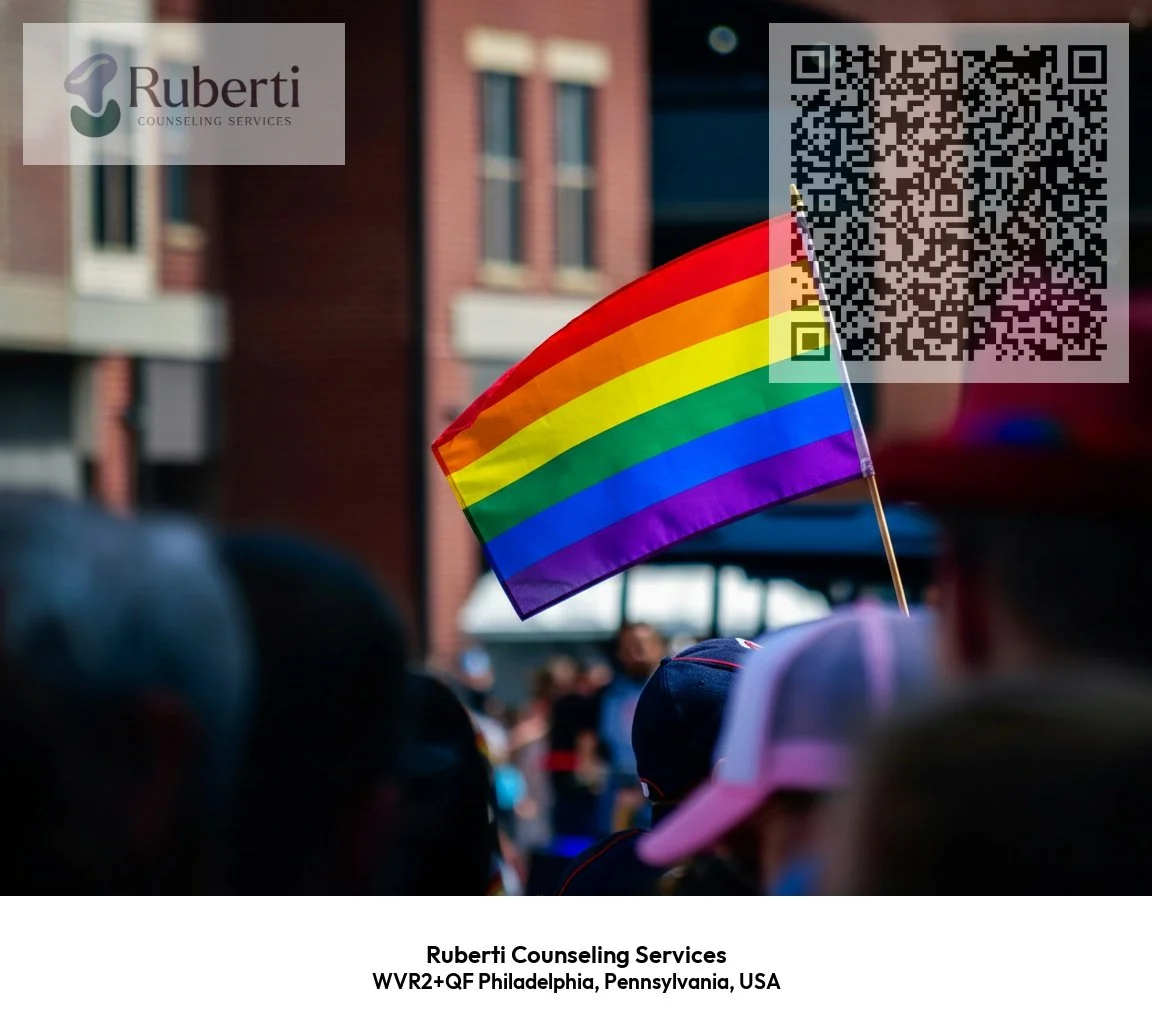 A crowd at an outdoor event with a rainbow pride flag being held up. The setting is urban with brick buildings in the background. There is a QR code and a semi-transparent logo of Ruberti Counseling Services in the top left corner.