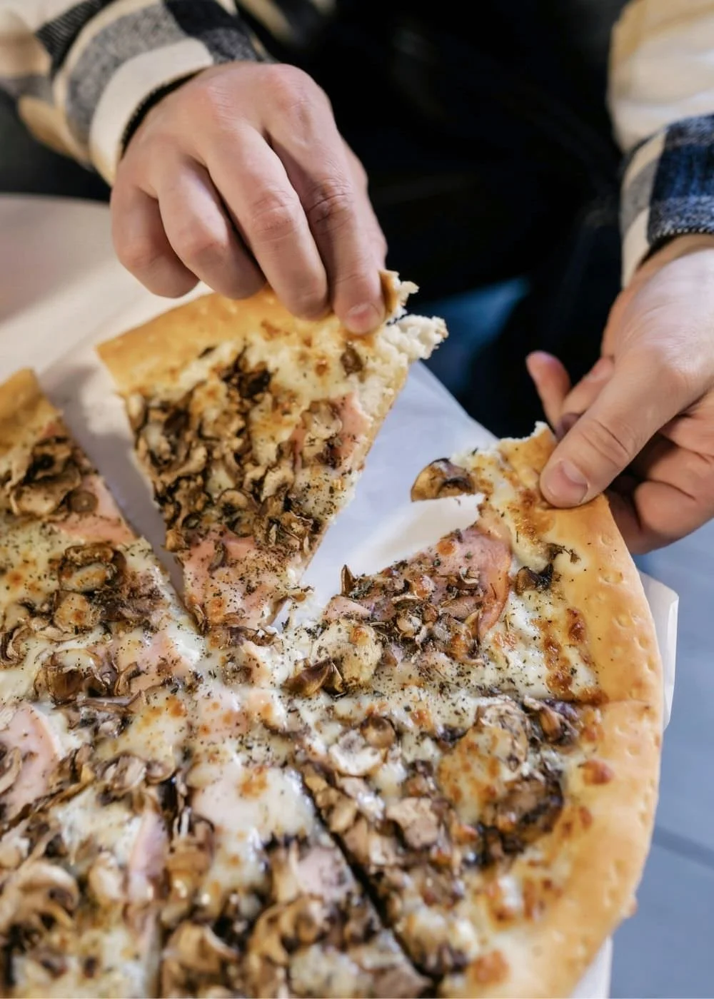 A picture of a pizza with toppings and a hand grabbing a slice.