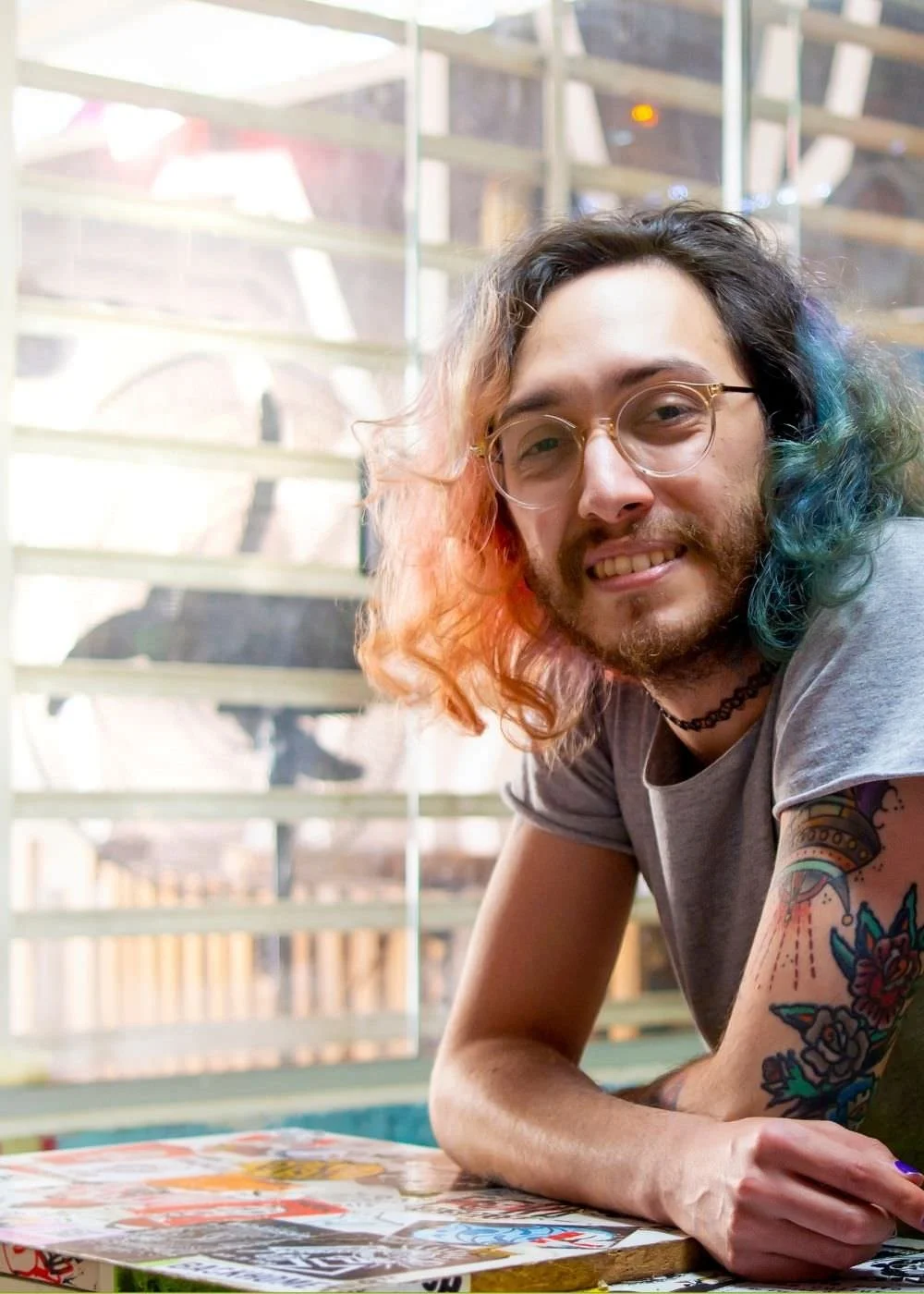 A picture of a queer, gender non-conforming person with colored hair and tattoos.