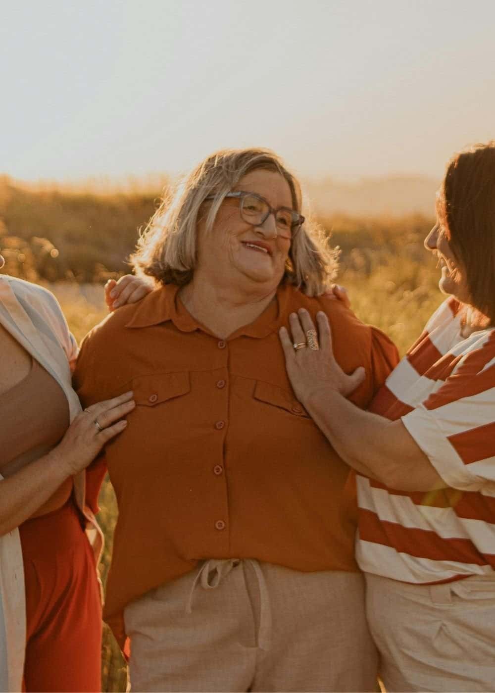 A picture of three middle-aged women hugging at a field.