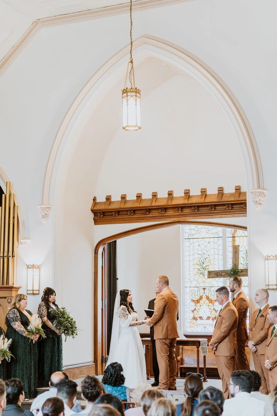 A wedding ceremony inside a church with the bride and groom standing at the altar, surrounded by bridal party and guests.