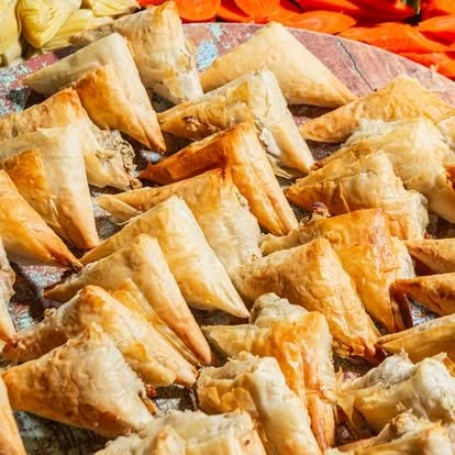 A large tray filled with fried samosas, a triangle-shaped Indian snack with a crispy golden exterior.