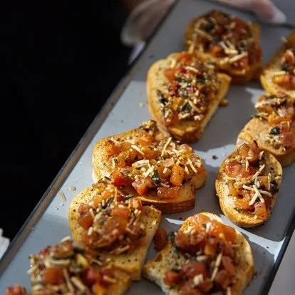 Close-up of toasted baguette slices topped with tomato mixture and shredded cheese on a tray.