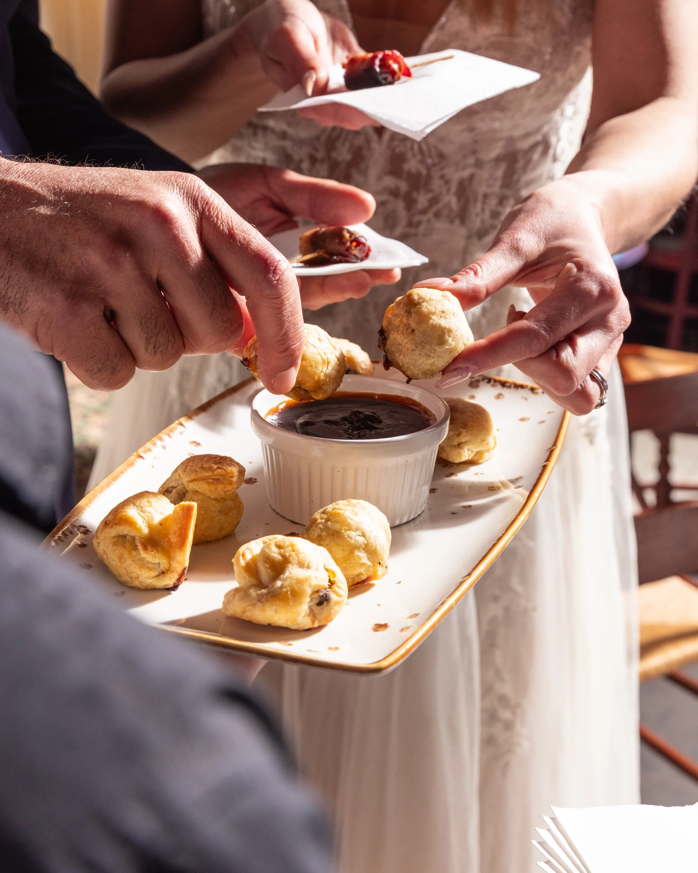 People sharing a plate of various appetizers with a bowl of dipping sauce at a social gathering.