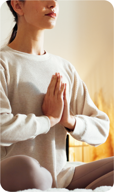 A woman practicing meditation or yoga indoors with hands in prayer position.