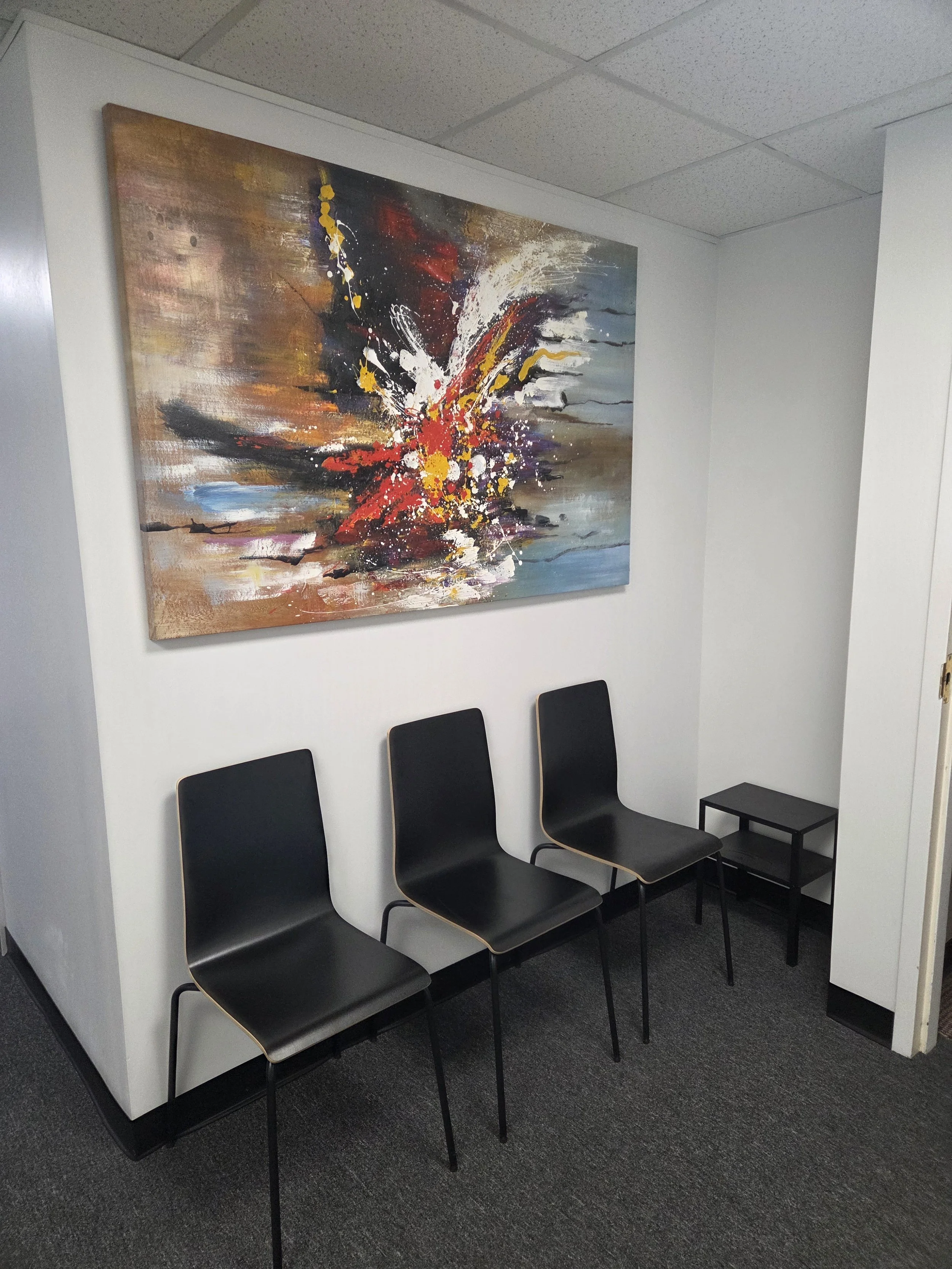 Kaleidoscope Counseling & Consulting, LLC waiting room. Three black chairs with wooden trim line a wall under a large abstract painting in an office or waiting room.