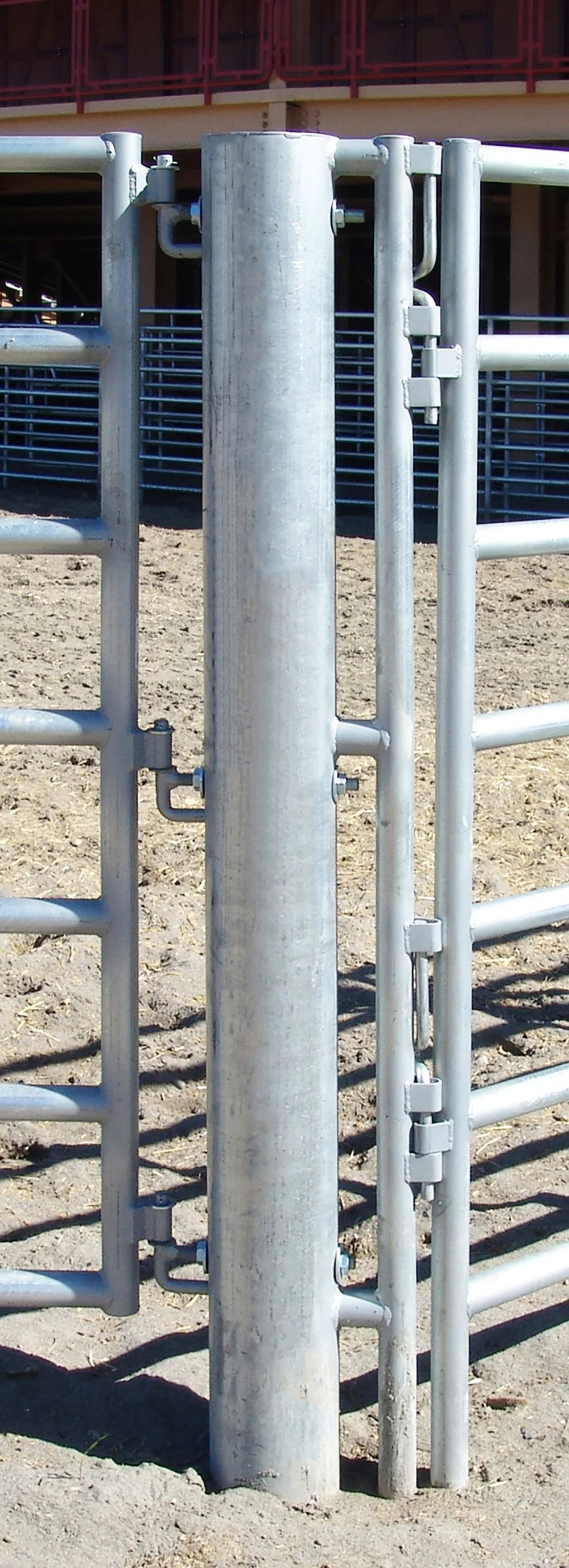 Close-up of a metal gate and fence at a construction site or outdoor area with dirt ground and a building in the background.