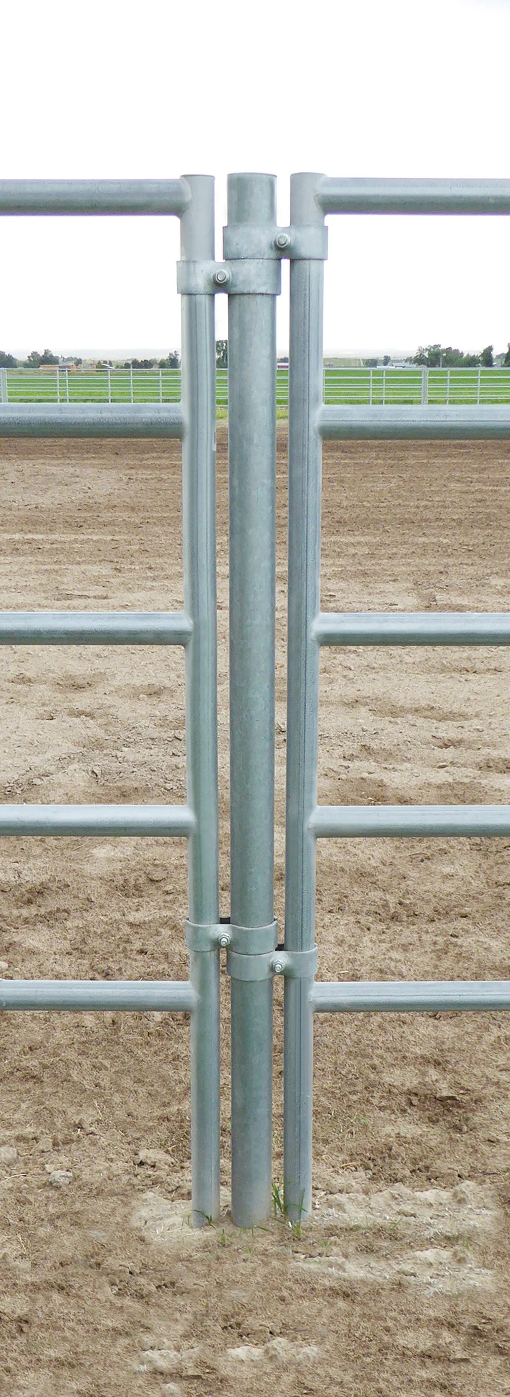 Metal gate at the entrance to a dirt arena, with green fields and fencing in the background.
