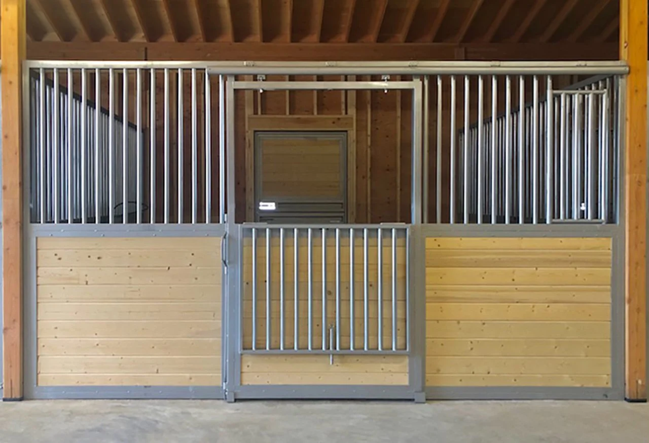 A horse stall with a wooden lower panel, metal upper bars, and a metal door in a barn.