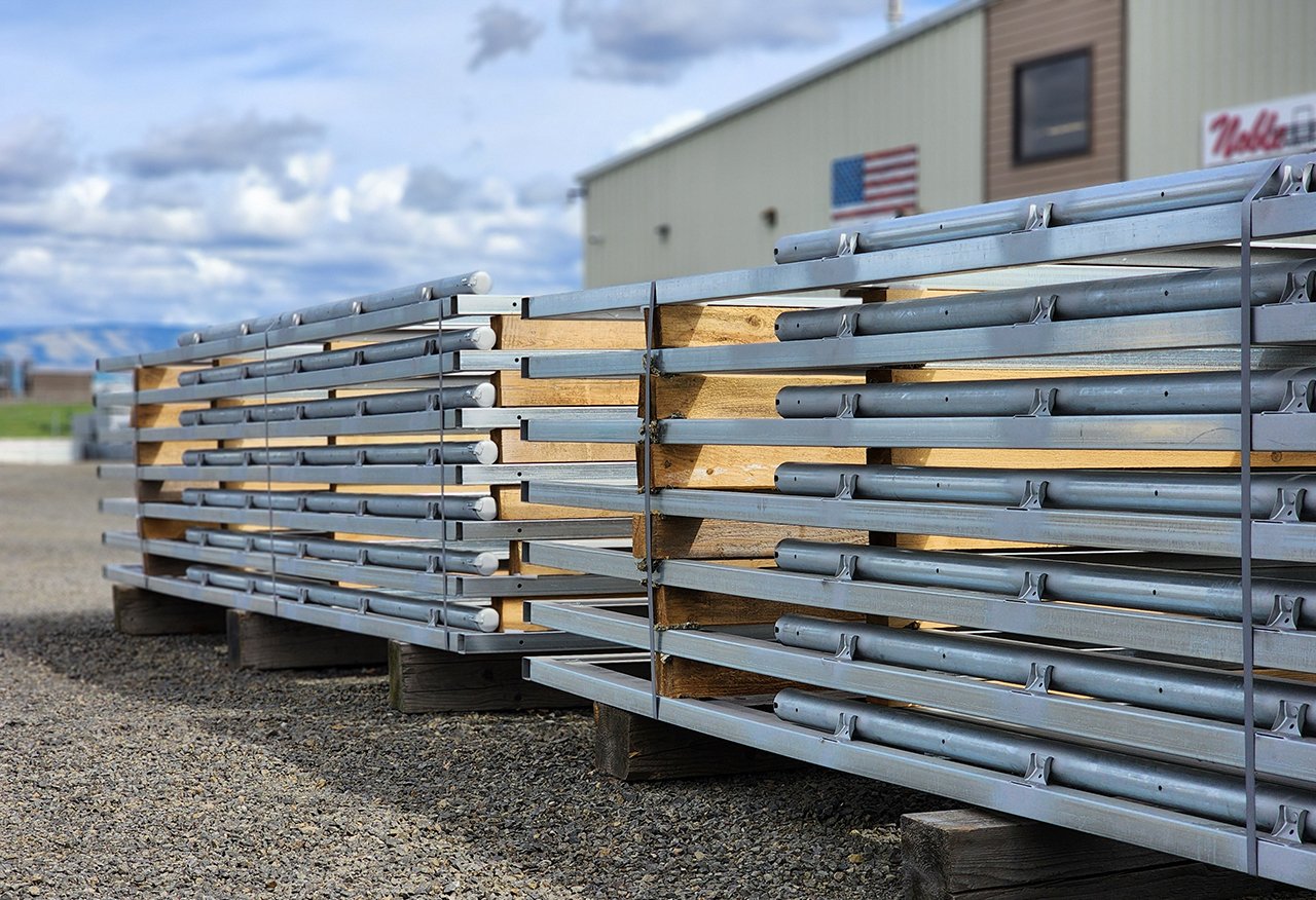 Multiple metal and wooden poles stacked on pallets outdoors.
