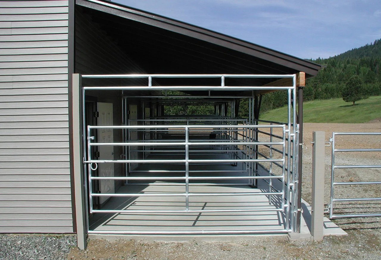 Metal livestock pens attached to a barn, with rolling hills and trees in the background.