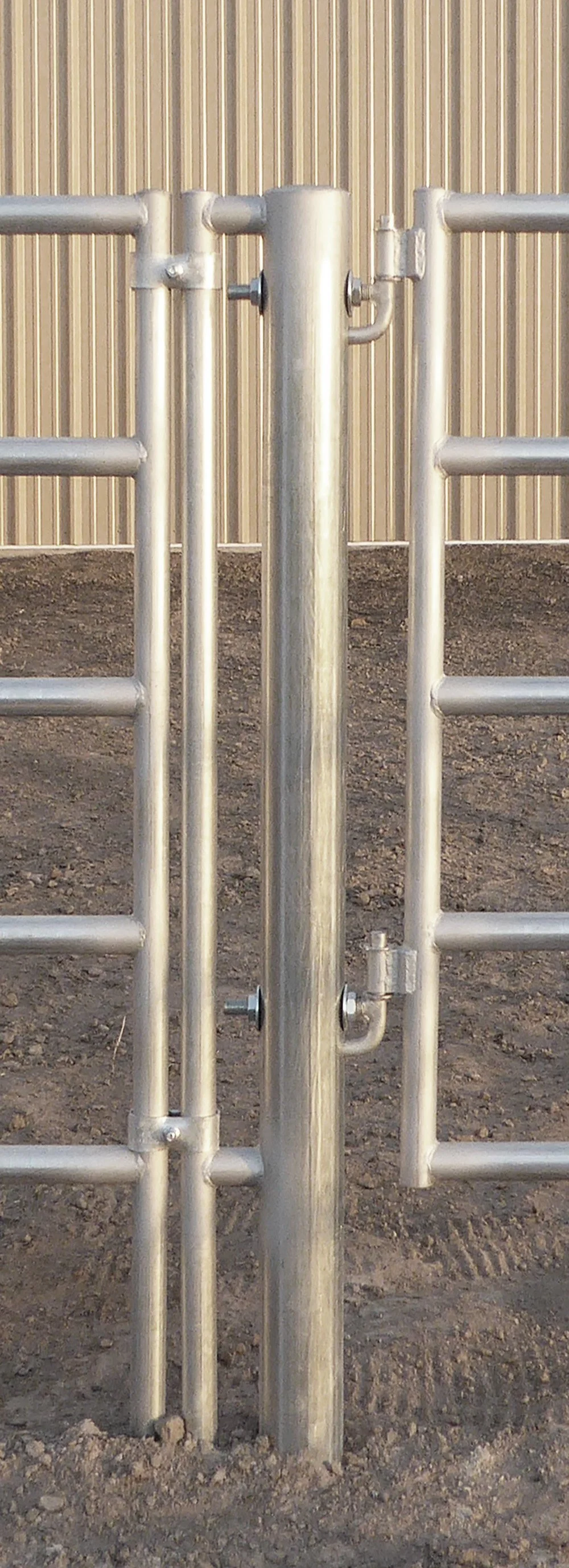 Metal gate with horizontal bars and vertical poles, set on dirt ground with a corrugated metal wall in the background.