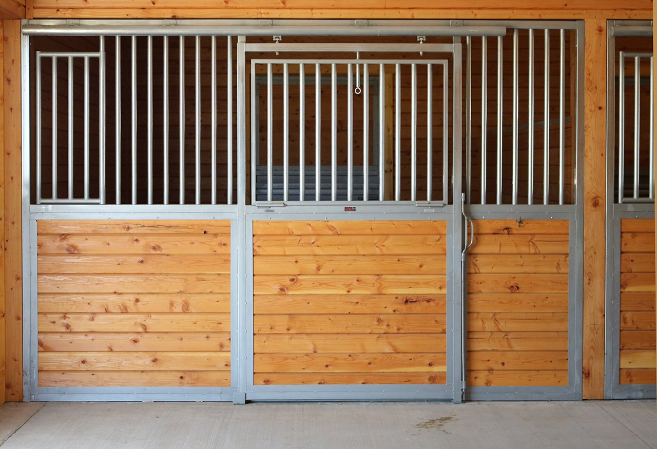 Image of horse stall doors with wooden lower panels and metal upper frames inside a stable or barn.