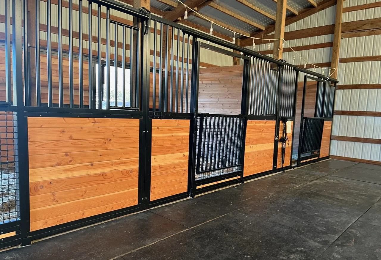 Interior view of horse stalls with wooden and black metal doors in a barn.