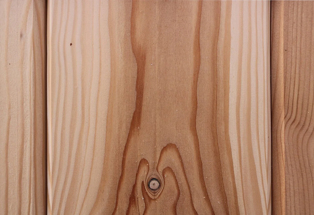 Close-up photo of a wood panel with visible grain, knots, and natural coloring.