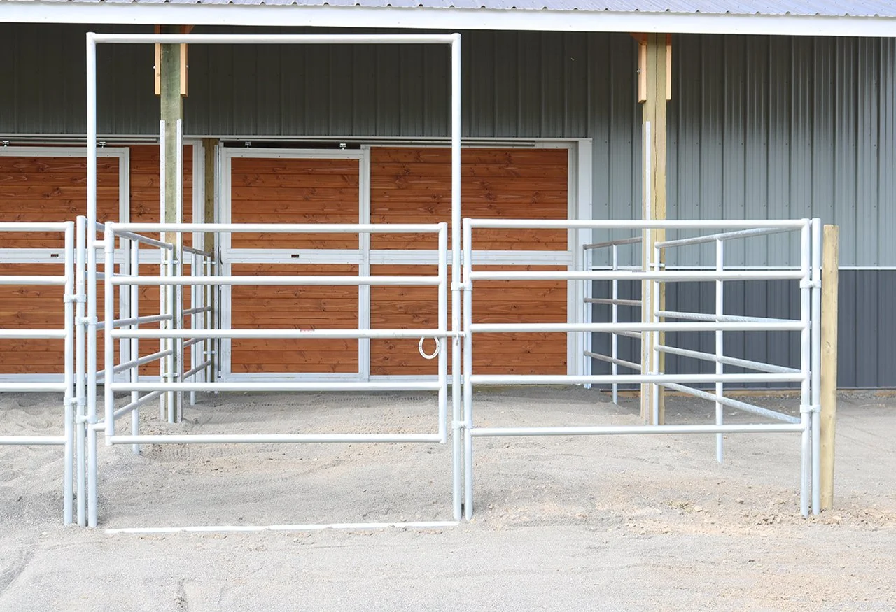 Empty horse stall with white metal railings in front of a wooden wall inside a barn.