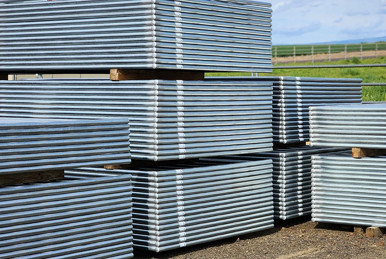 Stacks of metal pipes or poles organized in bundles outdoors on wooden pallets with a rural landscape in the background.