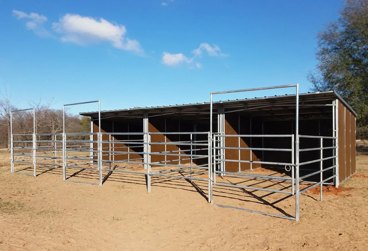 A small outdoor animal shelter with metal fencing on dirt ground, under a blue sky with a few clouds, surrounded by trees.