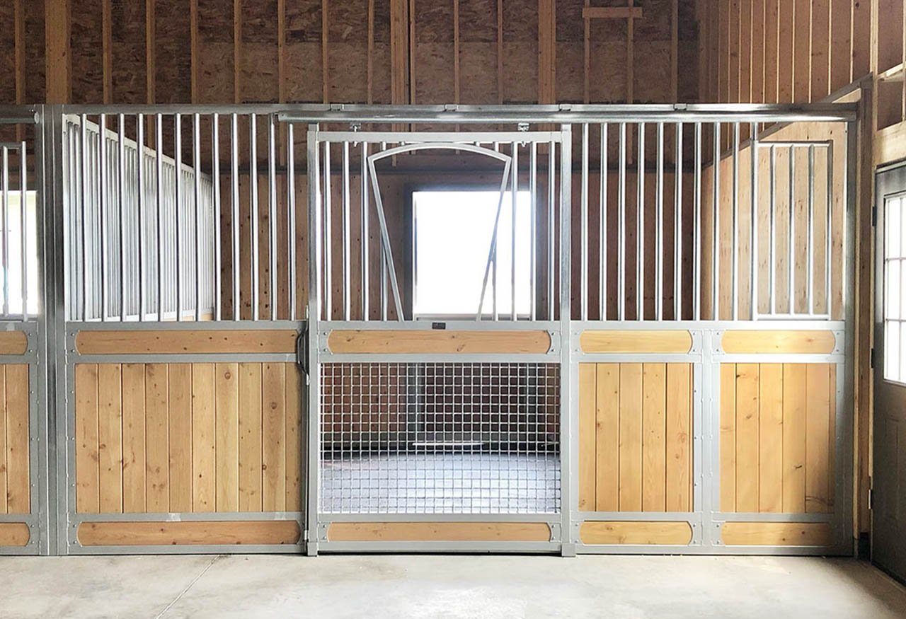 A wooden and metal horse stall with a small window at the back inside a barn.