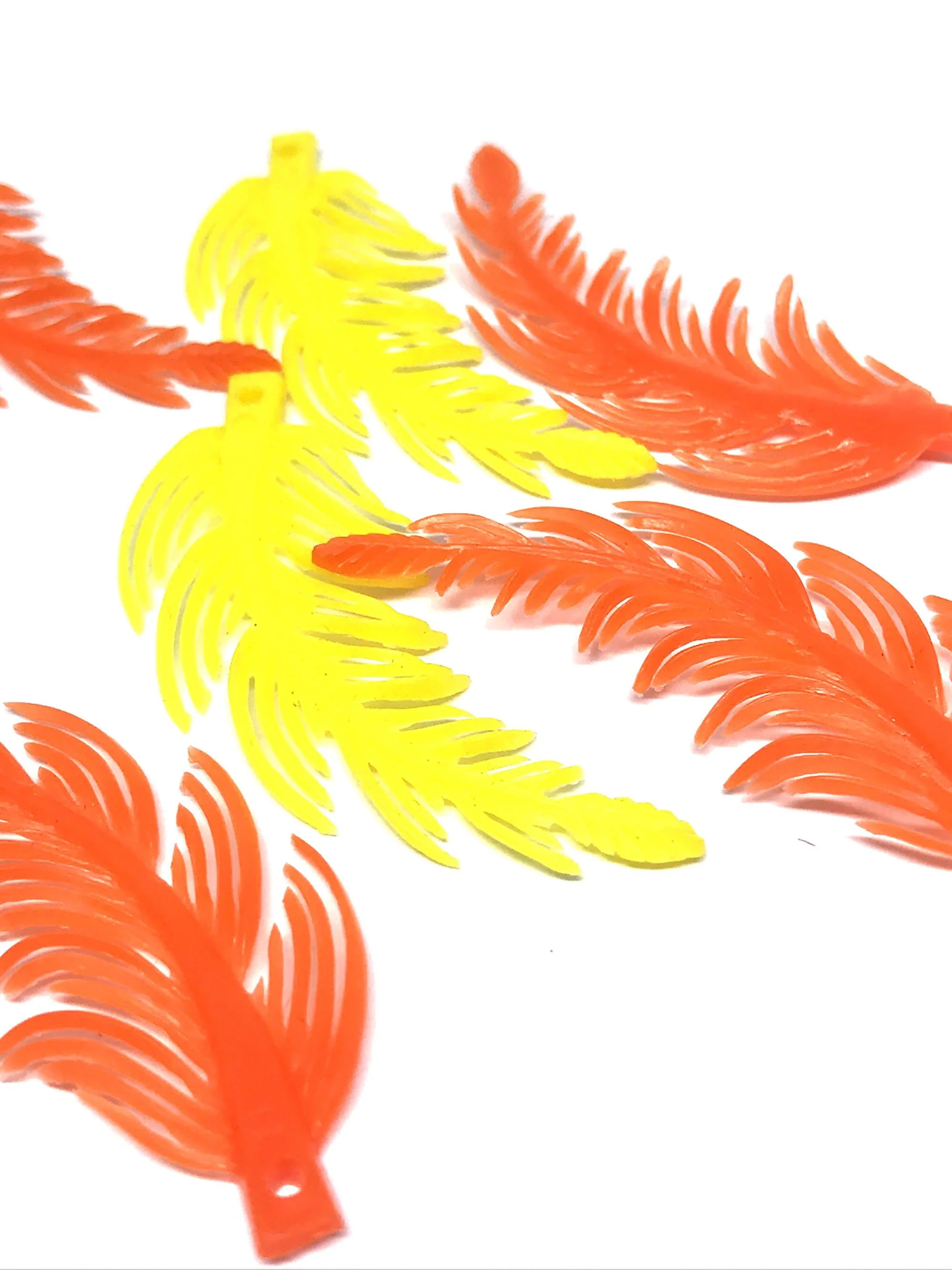 Colorful plastic feather-shaped pendants in orange and yellow arranged on a white surface.