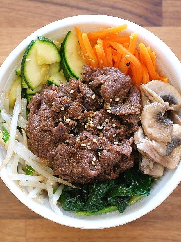 Bowl of vegetable and beef stir-fry with cucumber, carrots, mushrooms, spinach, bean sprouts, and sesame seeds.