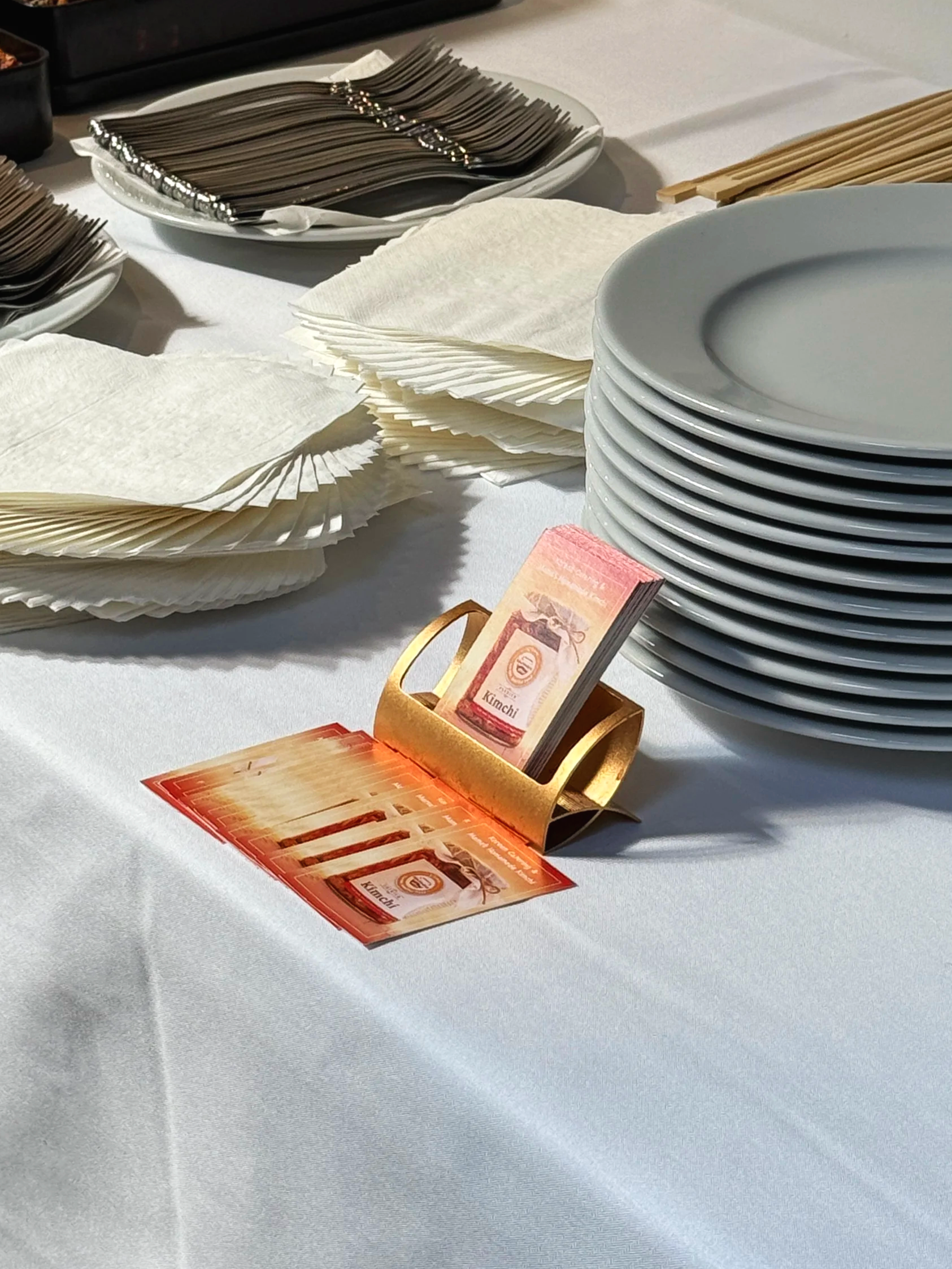 A table set for a meal with white napkins, black, beige, and gray plates, and a gold napkin holder with restaurant coupons or vouchers in a restaurant or banquet setting.