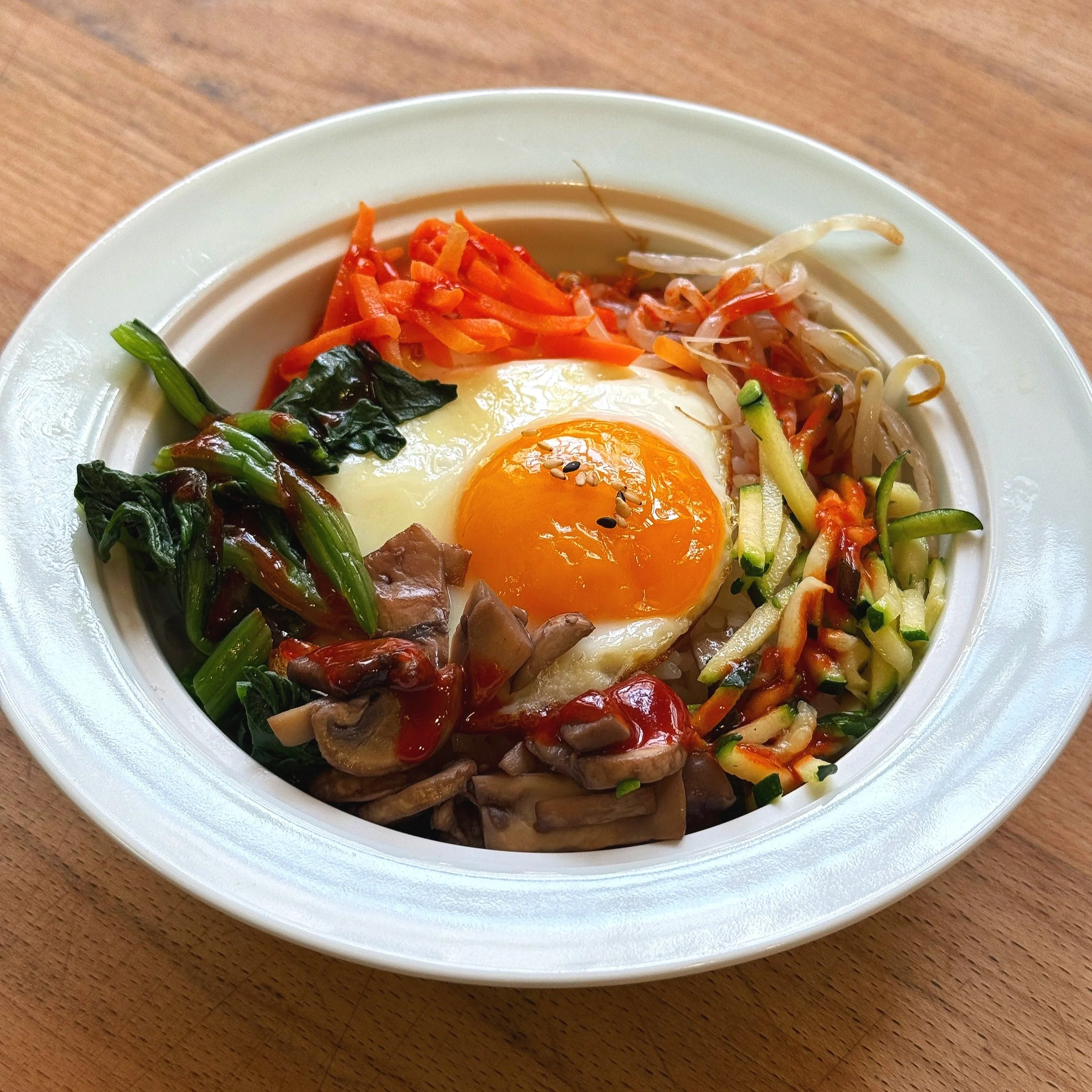 Bowl of Korean bibimbap with a fried egg on top, assorted vegetables, and sauce.