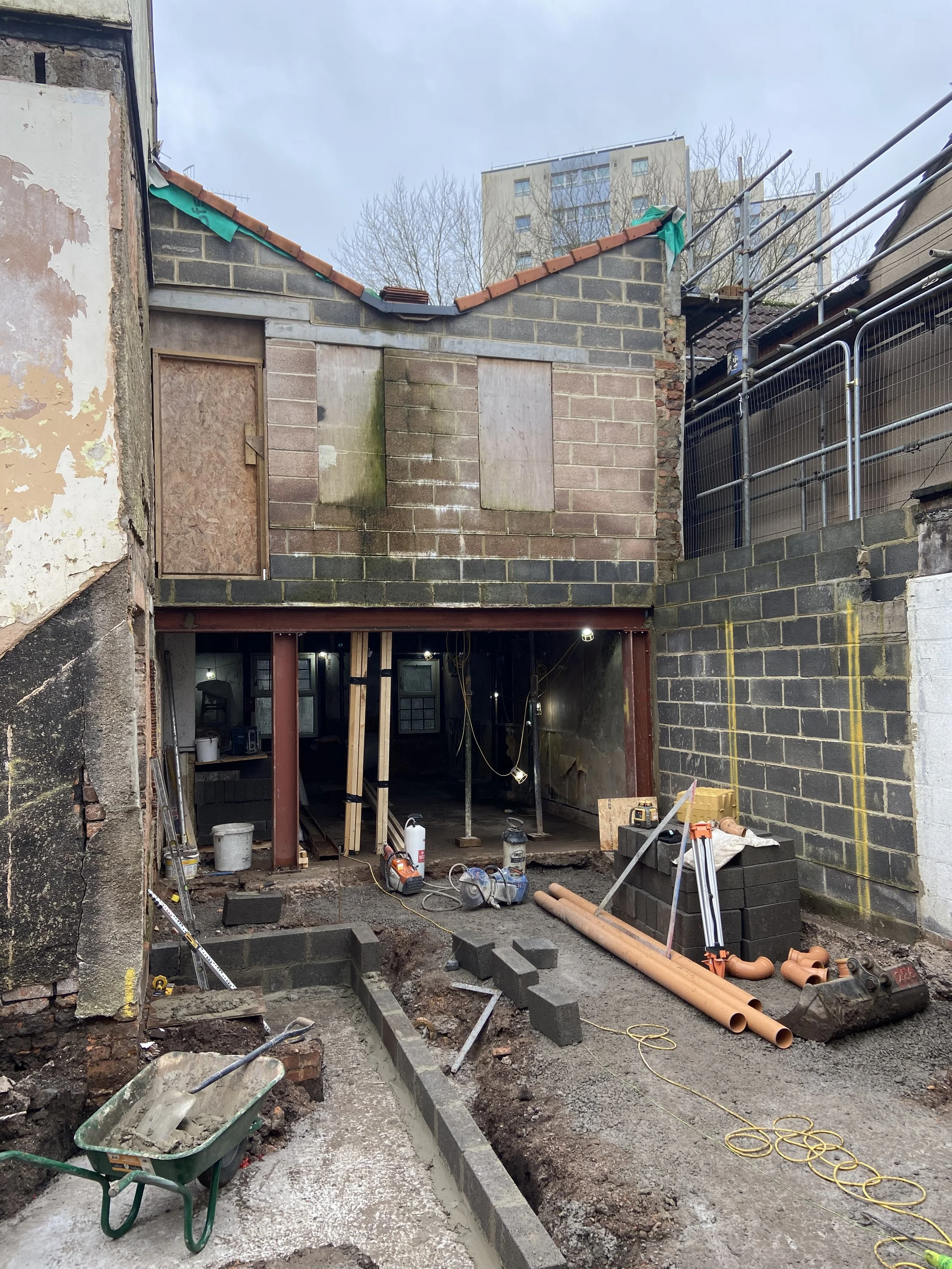 Construction site with building renovation in progress, showing partially demolished ground floor, construction tools, pipes, and materials.