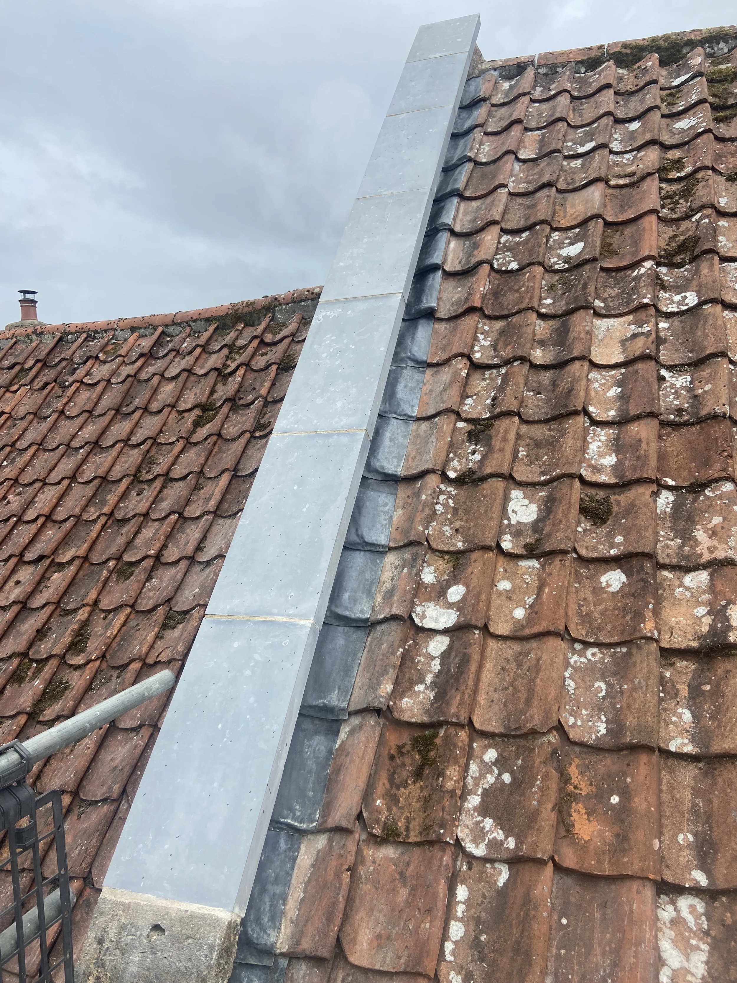 A section of a rooftop with traditional clay tiles and a metal flashing installed along the ridge for weatherproofing.
