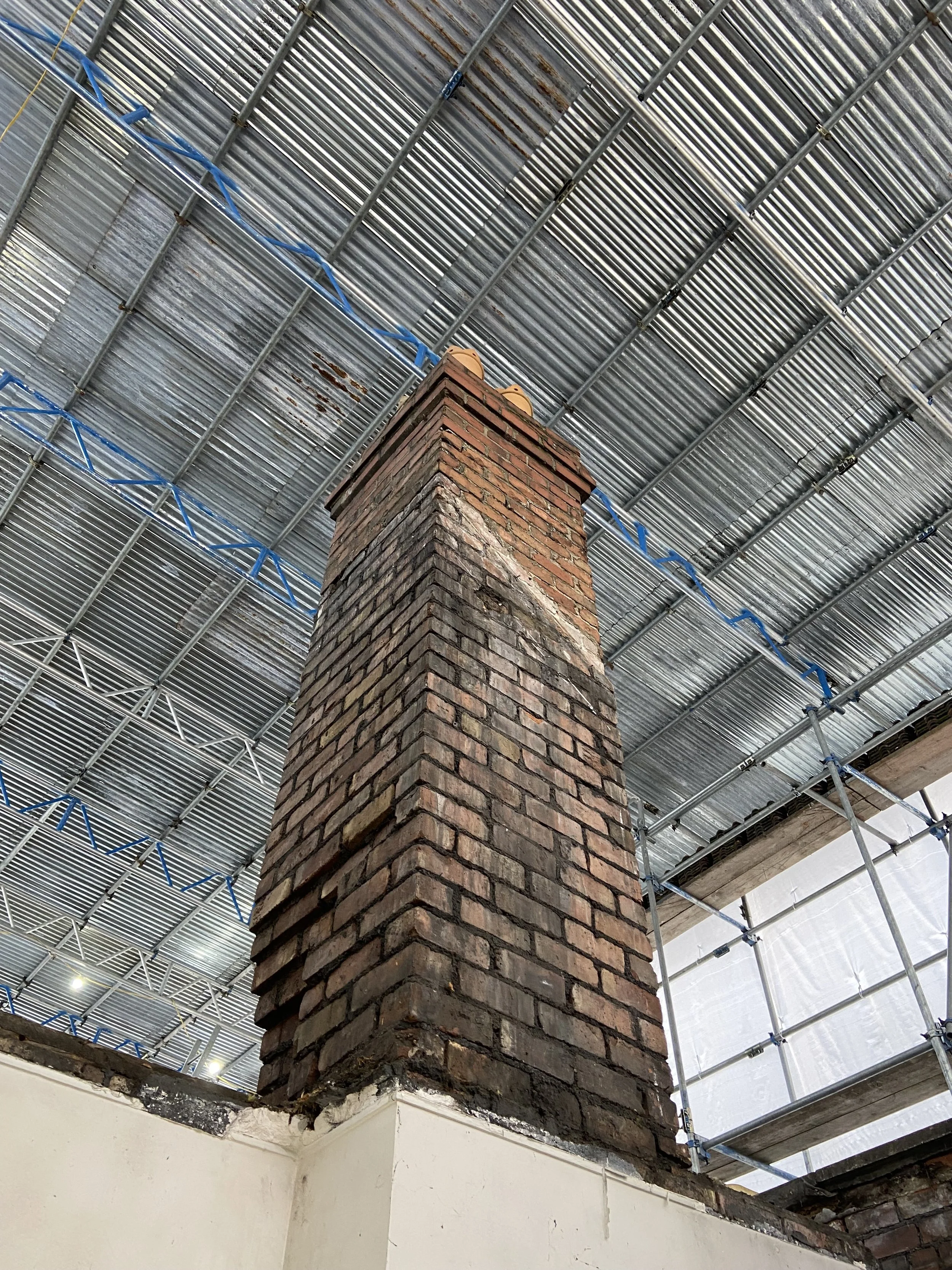 A brick chimney on top of a building, surrounded by construction scaffolding and a metal roof overhead.