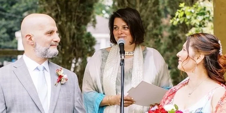 Wedding officiant officiating a wedding ceremony at an outdoor venue with a bride and groom listening.