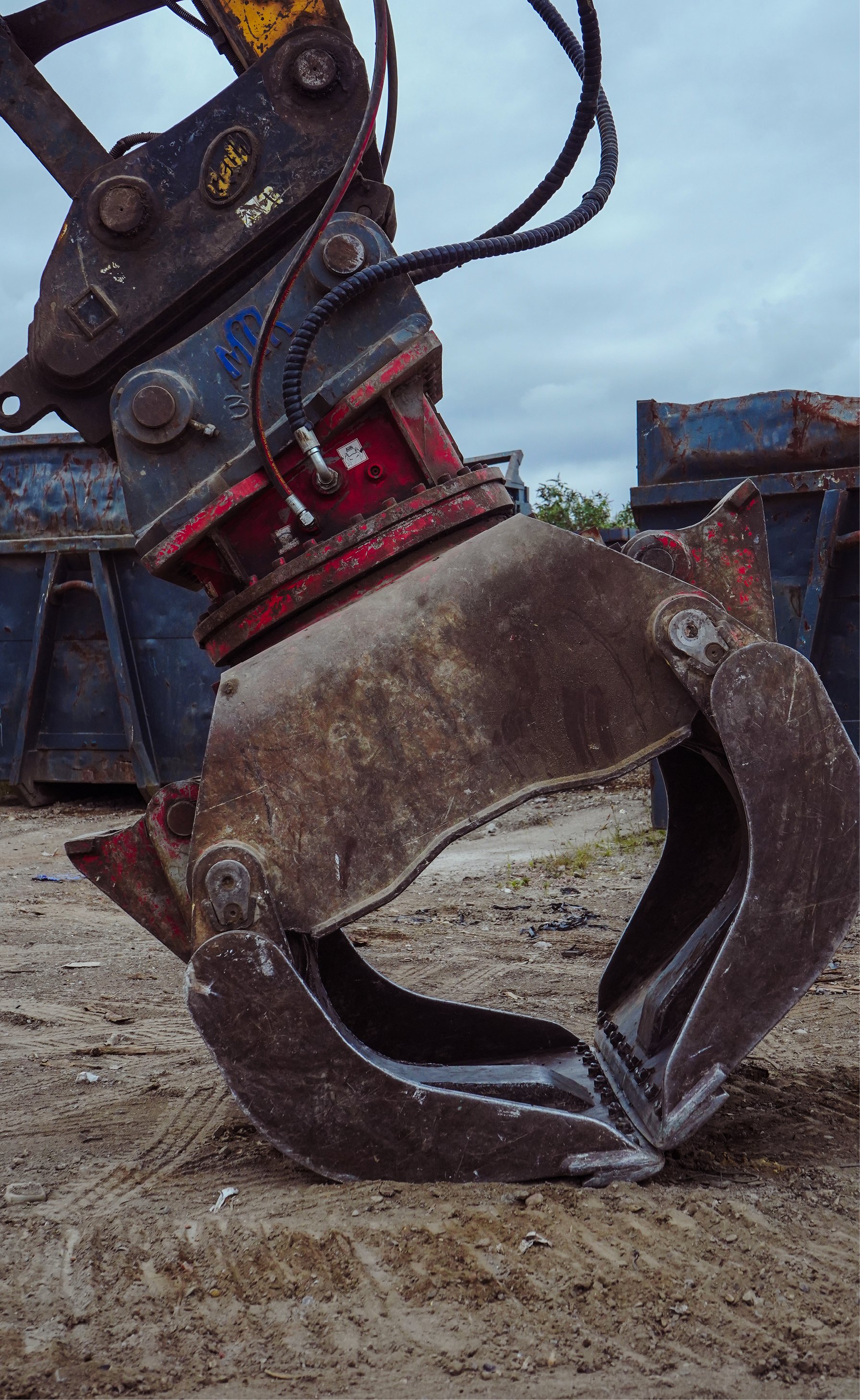 Metal claw attachment of an excavator on dirt ground with industrial background.