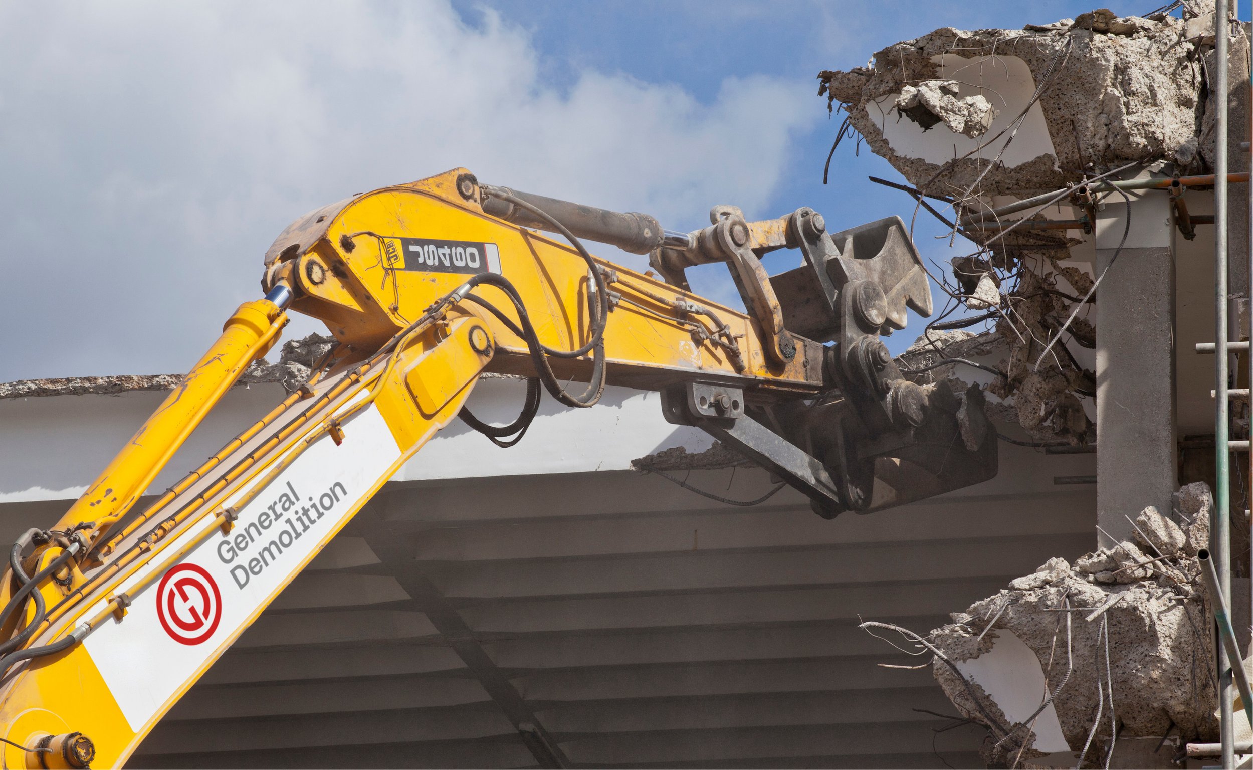 Yellow excavator arm demolishing a concrete structure with exposed rebar.