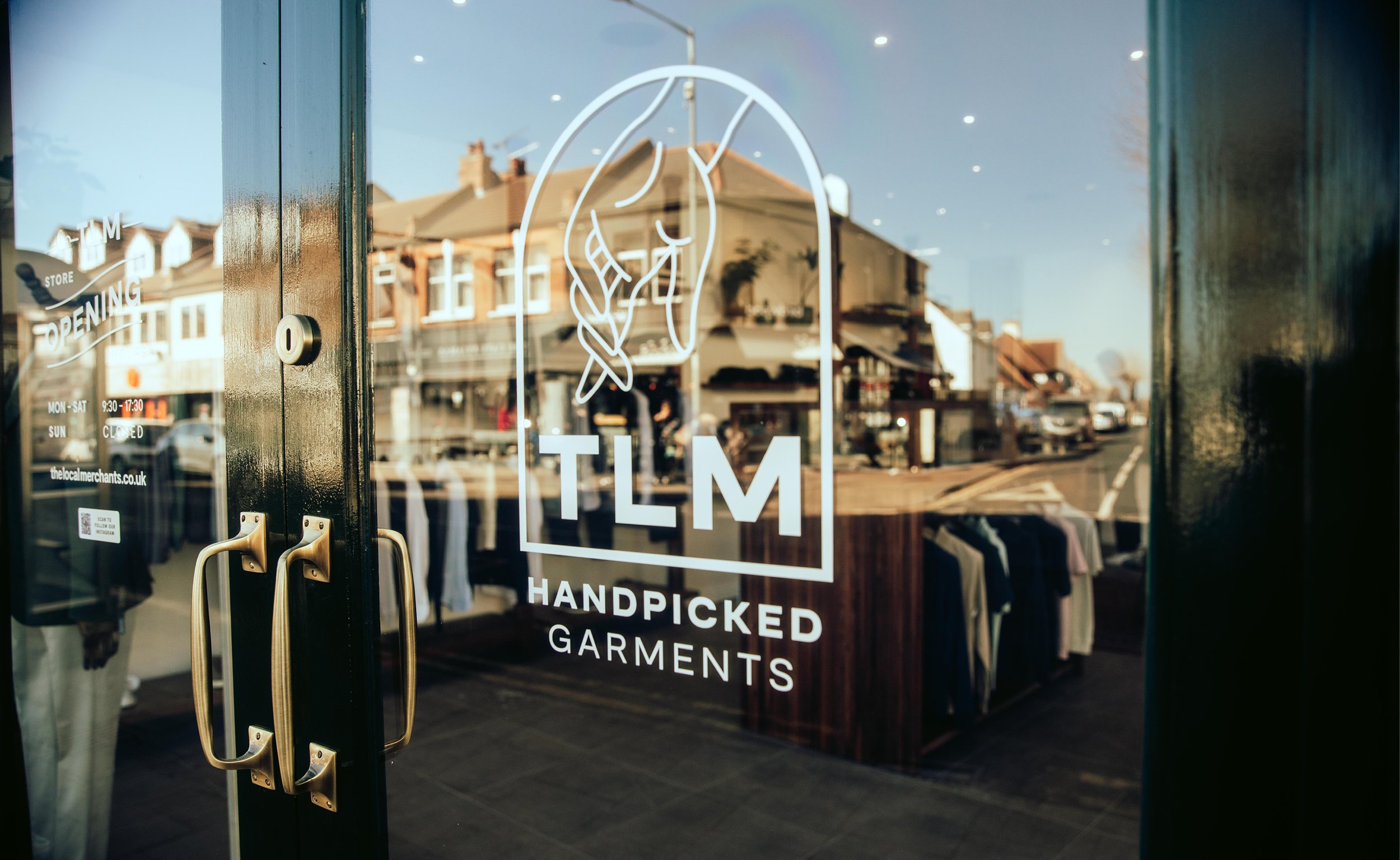 Shop door with "TLM Handpicked Garments" logo, clothing racks visible inside, street reflection on glass.
