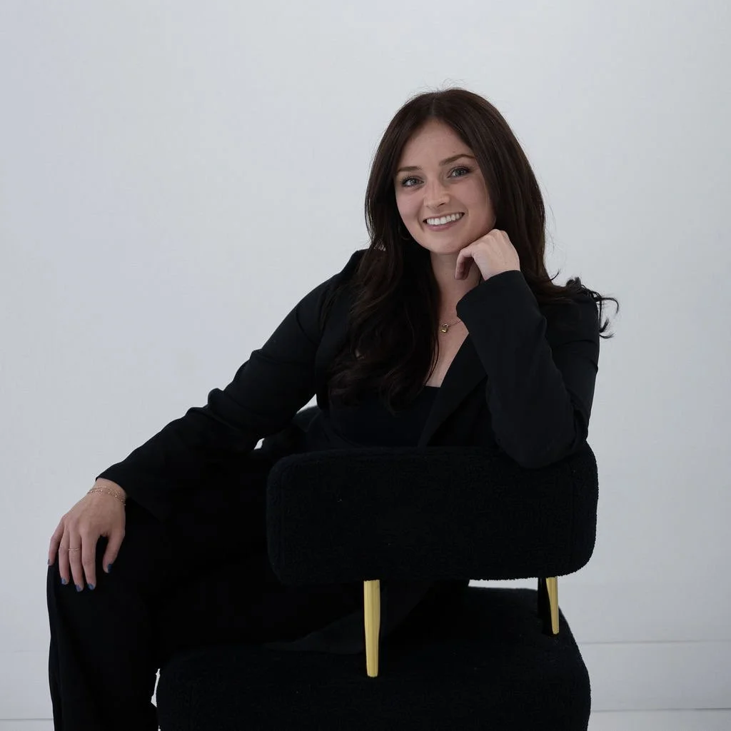 young woman smiling, wearing a black pant suit, brown hair