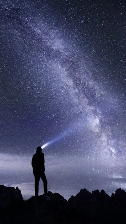 Night time silhouette of a hiker shining a headlamp towards the starry sky
