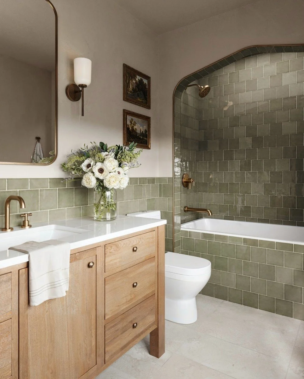 This image shows a beautiful bathroom with green tile, and a light wood vanity.