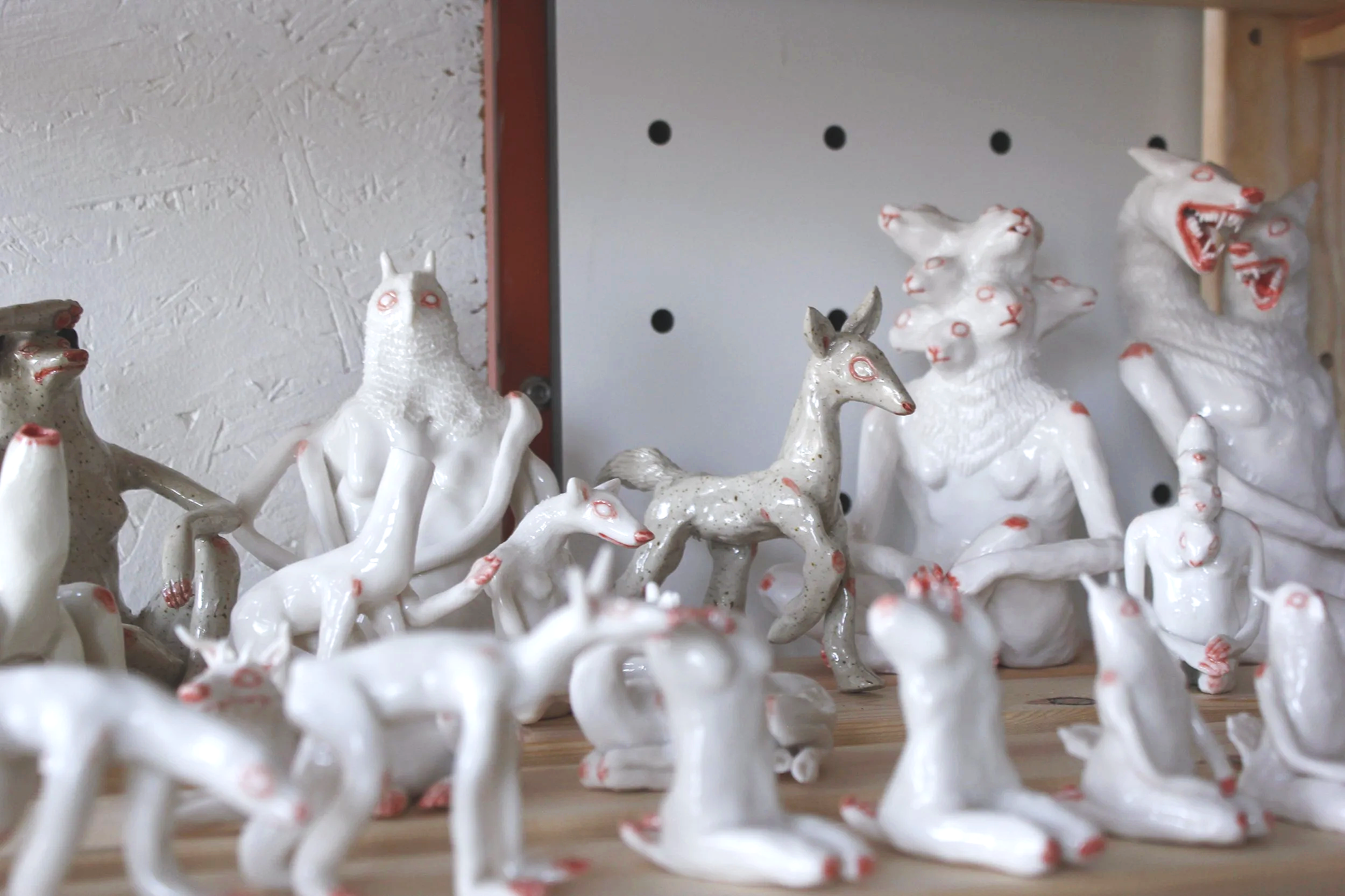 Collection of white ceramic animal figurines, including rabbits, foxes, and other creatures, displayed on a wooden surface against a white and red wall.